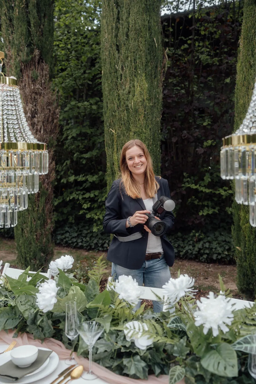Anna-Lena Woll, Hochzeitsfotografin, mit Kamera und Blitz zwischen Zypressen und Blumendekoration